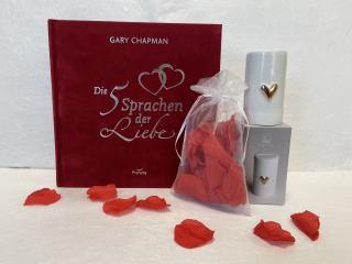 Rote Rosenblätter in weißem Organza-Sackerl, weiße Porzellan-Spardose mit goldenem Herz, Buch von Gary Chapmann mit dem Titel Die fünf Sprachen der Liebe