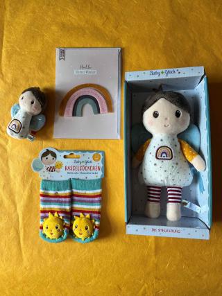 Minirassel in Form einer Stoffpuppe, Rasselsöckcken mit bunten Streifen und einer Sonne, Billett mit dem Aufdruck Hallo kleines Wunder, Stoffpuppe.