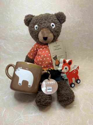 Brauner Plüschteddy mit rotem Shirt mit weißen Punkten; braune Tasse mit einem Eisbären; kleines Holzreh mit Rädern